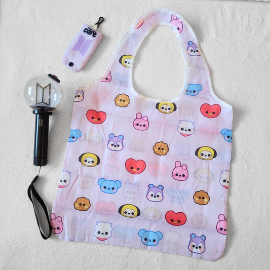 A light-purple tote bag with BTS's BT21 characters on a white background. A 5th generation bts lightstick is on the left side. The tote storage clip-on bag is on the top-left of the image.